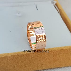 May include: A rose gold hammered band ring. The ring is wide and has a textured surface.