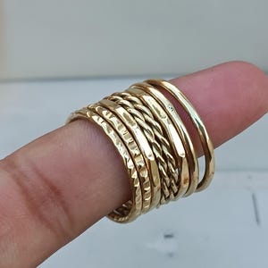 May include: A set of eight gold-toned stacking rings. The rings are made of different textures, including hammered, twisted, and smooth.