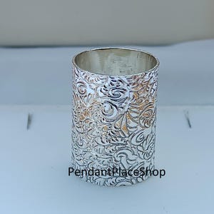 May include: A silver ring with an ornate floral design. The ring is cylindrical and has a detailed embossed pattern. The text "PendantPlaceShop" is at the base of the ring.