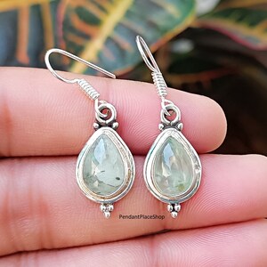 May include: A pair of silver teardrop earrings with green gemstone accents. The earrings have a delicate design and are perfect for everyday wear.