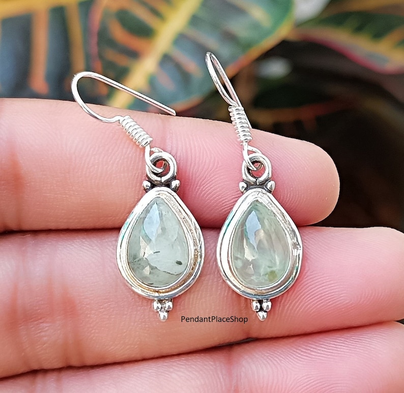 May include: A pair of silver teardrop earrings with green gemstone accents. The earrings have a delicate design and are perfect for everyday wear.