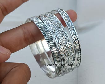 May include: Set of four silver bangles with intricate floral designs. The bangles are stacked on top of each other and have a shiny finish.