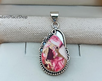 May include: A teardrop-shaped pendant with a silver bail. The pendant features a pink, white, and gold stone with a silver bezel and decorative edging. The stone has a unique, marbled appearance. The pendant is likely for a necklace.