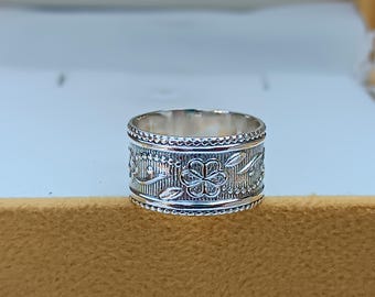 May include: A silver ring with a floral design. The ring is wide and has a textured surface.