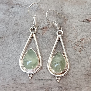 May include: A pair of silver teardrop earrings with green gemstone accents. The earrings have a delicate, openwork design and feature a small, beaded detail at the bottom.
