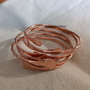 Peut inclure: Cinq bracelets en cuivre empilés les uns sur les autres. Les bracelets sont fins et ont une texture légèrement martelée. Les bracelets sont tous de la même taille et de la même forme. PendantPlaceShop est écrit en blanc sur le bracelet du haut.