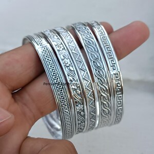 Op de afbeelding: Set van zes zilveren armbanden met ingewikkelde gegraveerde ontwerpen. Elke armband heeft een ander patroon, waaronder bloemmotieven, geometrische patronen en golfmotieven.