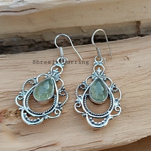 May include: A pair of silver earrings with a green gemstone in the center of each earring. The earrings have a delicate, ornate design.