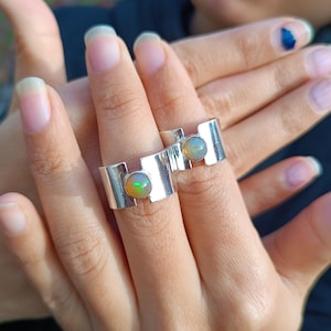 Op de afbeelding: Twee zilveren ringen met opaal edelstenen. De ringen hebben een uniek geometrisch ontwerp met een rechthoekige vorm en een gebogen gedeelte.