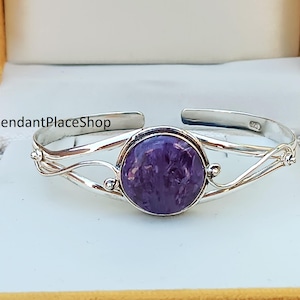 Pode incluir: Um bracelete de prata com uma pedra preciosa roxa engastada em um bezel de prata. O bracelete tem um design delicado e torcido.