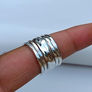 May include: A set of five silver stacking rings with a hammered texture. The rings are worn on a finger.