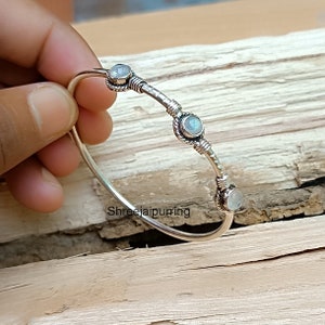 Pode incluir: Pulseira de prata com três pedras redondas de pedra da lua. A pulseira é feita de fio torcido e tem um design simples.