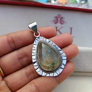 May include: A silver pendant featuring a green and white gemstone set within a silver and copper frame. The pendant is shaped like a teardrop.