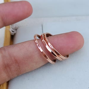 Peut inclure: Trois fines bagues en m&eacute;tal martel&eacute; or rose superpos&eacute;es sur un doigt.