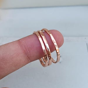 May include: Three thin, hammered, rose gold rings stacked on a finger.