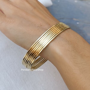 May include: A set of gold-toned bangle bracelets stacked on a person's wrist. The bracelets are smooth and have a shiny finish.