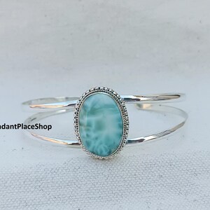 Peut inclure: Un bracelet en argent avec un cabochon ovale bleu clair serti dans une bélière en argent. La pierre précieuse a un motif tourbillonnant.