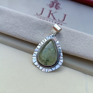 May include: A silver pendant featuring a green gemstone set in a teardrop shape. The pendant has an intricate silver border with a rope design.