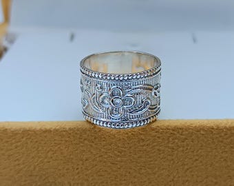May include: A silver ring with a floral design. The ring is wide and has a textured surface.