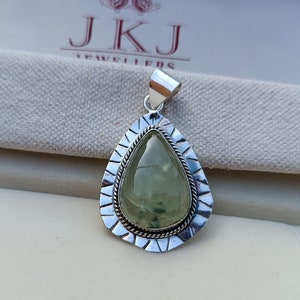 May include: A silver pendant featuring a green gemstone set within an intricate silver frame. The pendant is teardrop-shaped and has a silver bail for attaching a chain.