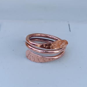 May include: A hammered copper ring with a twisted design. The ring is made of two bands of copper that are twisted together to create a unique and stylish look.