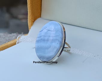 Könnte beinhalten: Ein Silberring mit einem großen, ovalen blau-Spitzenachat-Edelstein. Der Stein hat ein gebändertes Muster in Hellblau und Weiß. Der Ring ist in einem schlichten Silberband gefasst. Der Text "PendantPlaceShop" ist sichtbar.