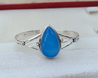 May include: A silver bracelet featuring a teardrop-shaped blue gemstone. The bracelet has a delicate, twisted design.