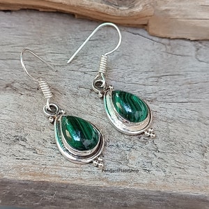 May include: A pair of silver earrings with green malachite teardrop-shaped stones. The earrings have a simple design with a silver hook and a small silver bead at the bottom.