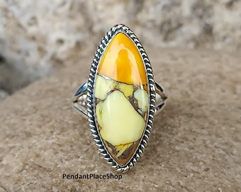 May include: A silver ring featuring an oval gemstone. The stone displays a blend of yellow, orange, and brown tones, with a textured surface. The ring has a twisted rope-style border. The text "PendantPlaceShop" is visible.