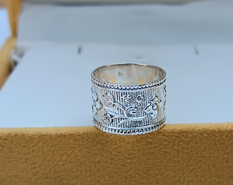May include: A silver ring with a floral design. The ring is wide and has a textured surface.