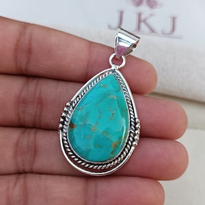 May include: A turquoise gemstone pendant with a silver setting. The pendant is in the shape of a teardrop and has a rope-like border.