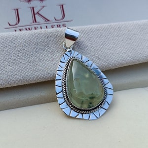May include: A silver pendant featuring a green gemstone set in a teardrop shape. The pendant has a detailed silver border with a rope-like design.