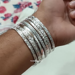 May include: A set of silver bangles with intricate designs. The bangles are stacked on a person's wrist. The bangles are all different sizes and have different patterns.