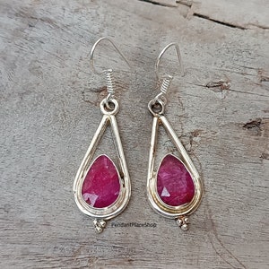 May include: A pair of silver dangle earrings with pink gemstone drops. The earrings have a teardrop shape and are accented with small silver beads.