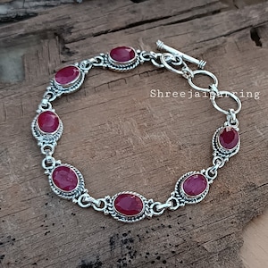 Op de afbeelding: Een zilveren armband met een schuifgesp heeft zes ovale, rode edelstenen die in zilver zijn gezet.
