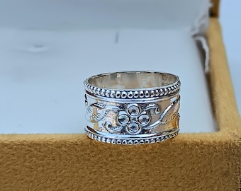 May include: A silver ring with a floral design. The ring has a beaded edge and a floral pattern with a central cluster of five round stones.