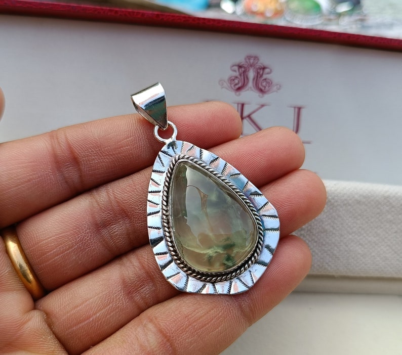 May include: A silver pendant featuring a green and white gemstone set within a silver and copper frame. The pendant is shaped like a teardrop.