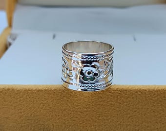 May include: Silver ring with a floral design. The ring is wide and has a textured surface.