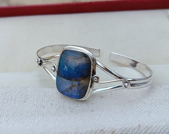 May include: A silver bracelet featuring a blue and green labradorite gemstone set in a silver bezel. The bracelet has a delicate, openwork design.