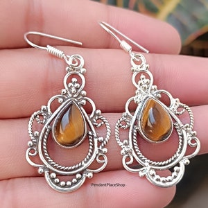 May include: Silver dangle earrings with a teardrop-shaped tiger's eye gemstone set in a filigree design. The earrings have a silver hook closure.
