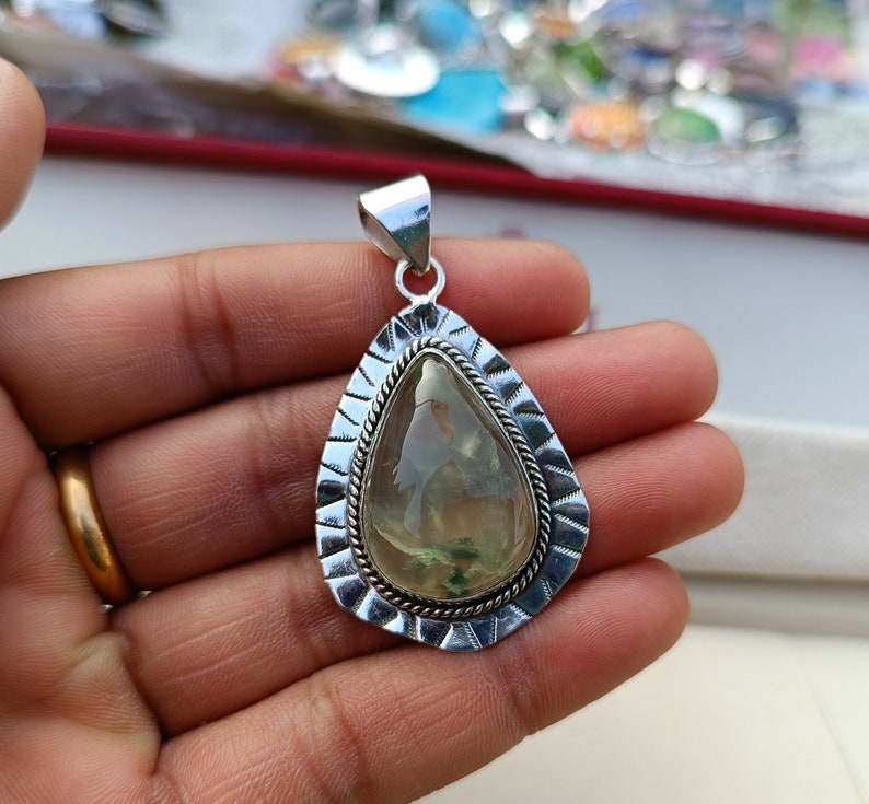 May include: A silver pendant featuring a green and white gemstone in a teardrop shape. The pendant has an intricate silver border.