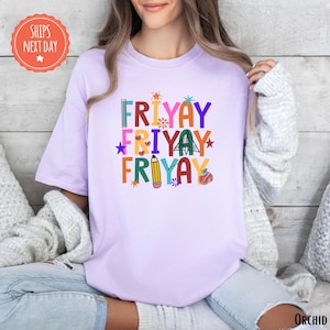 A woman wearing a pink t-shirt with a colorful graphic design that says "FRYAYAY FRYAYAY FRYAYAY" printed on it.