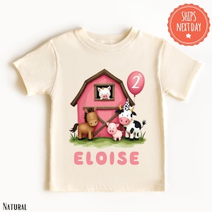 May include: A light beige t-shirt with a pink barn, a horse, a cow, two pigs, and a pink balloon with the number "2" on it. The text "ELOISE" is printed below the animals.