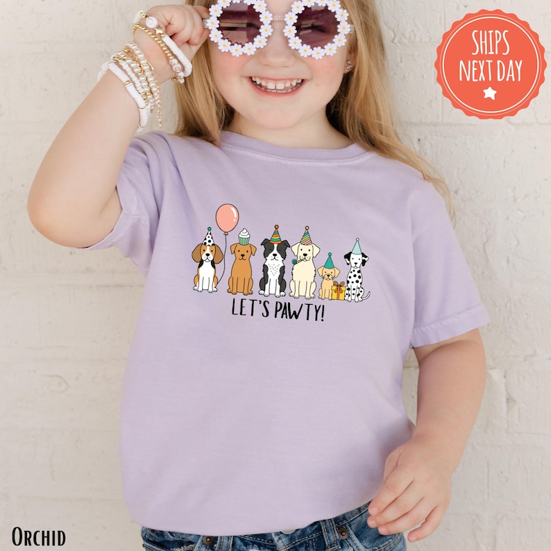 A young girl wearing a purple t-shirt with a graphic of cartoon dogs and the text "Let's pawty!"