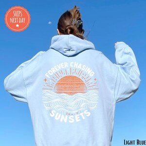 a woman wearing a white hoodie that says forever changing sunsets