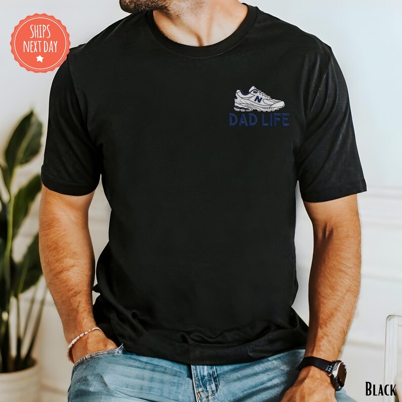 A man wearing a black t-shirt with a graphic design on the front, including a shoe and the text "DAD LIFE".