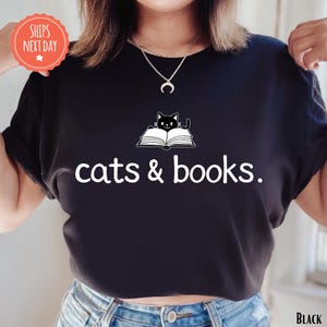 A person wearing a black t-shirt with the text "cats & books" printed on it, along with a cat graphic.
