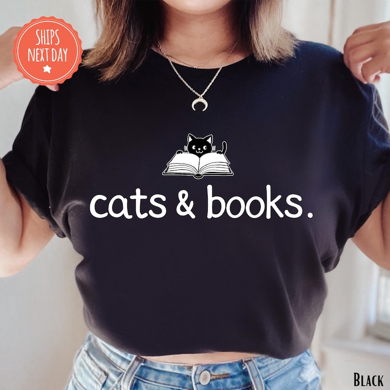 A person wearing a black t-shirt with the text "cats & books" printed on it, along with a cat graphic.