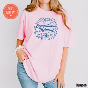A woman wearing a pink t-shirt with the text "Occupational Therapy" printed on it, standing against a white background.