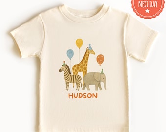 May include: Cream-colored toddler t-shirt featuring a watercolor illustration of a zebra, giraffe, and elephant, each wearing a party hat and holding balloons. The name "HUDSON" is printed in orange below the animals.